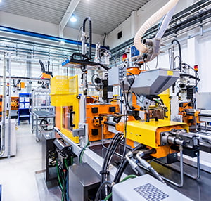 Horizontal color image of large group of automated injection moulding machines for plastic parts production. Powerful molding machinery in factory arranged in a row.